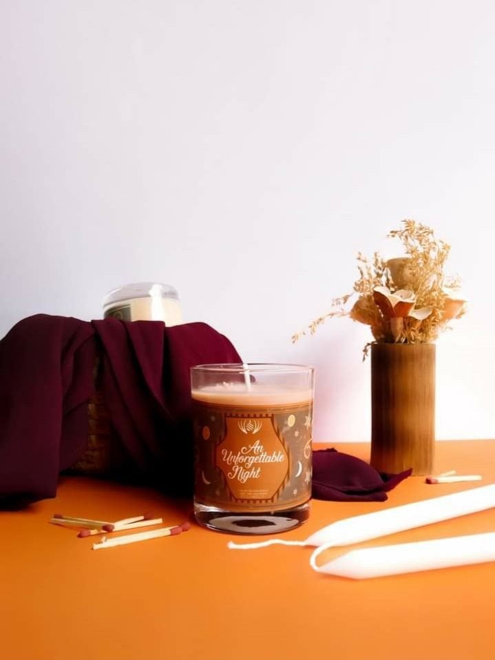 An Unforgettable Night candle: a brown label scattered with moons and stars, beside a burgundy cloth and matches.